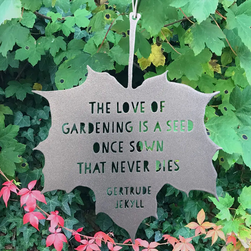 Metal leaf-shaped sign with gardening quote surrounded by green leaves