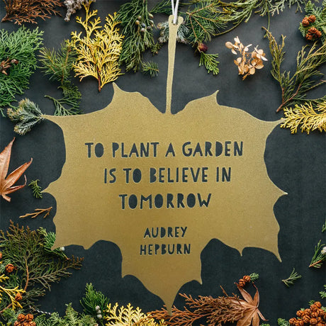 Gold leaf-shaped sign with Audrey Hepburn quote surrounded by greenery on a dark background